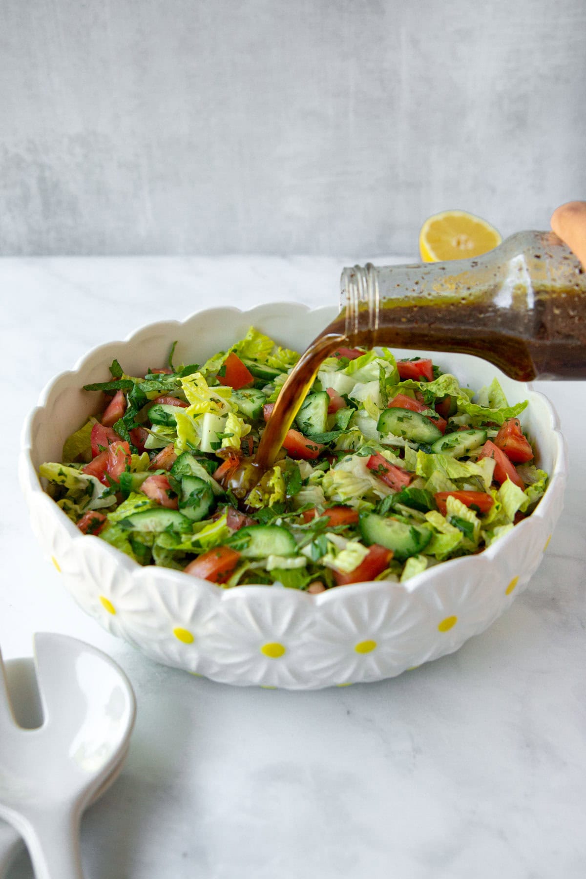 Fresh fattoush with salad dressing being poured from a glass bottle.