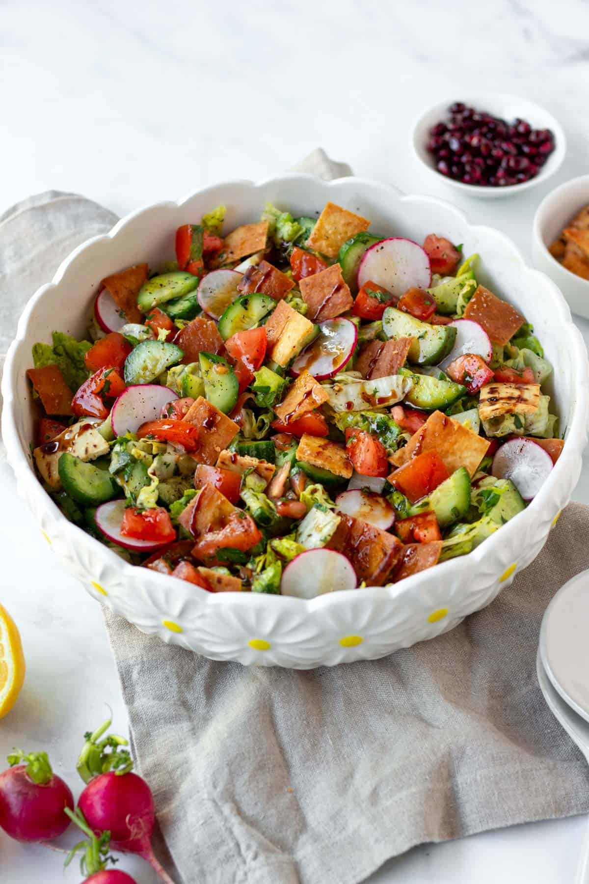 Fresh fattoush salad with radishes, cucumbers, tomatoes, and pita chips in a white bowl at a 45 degree angle.