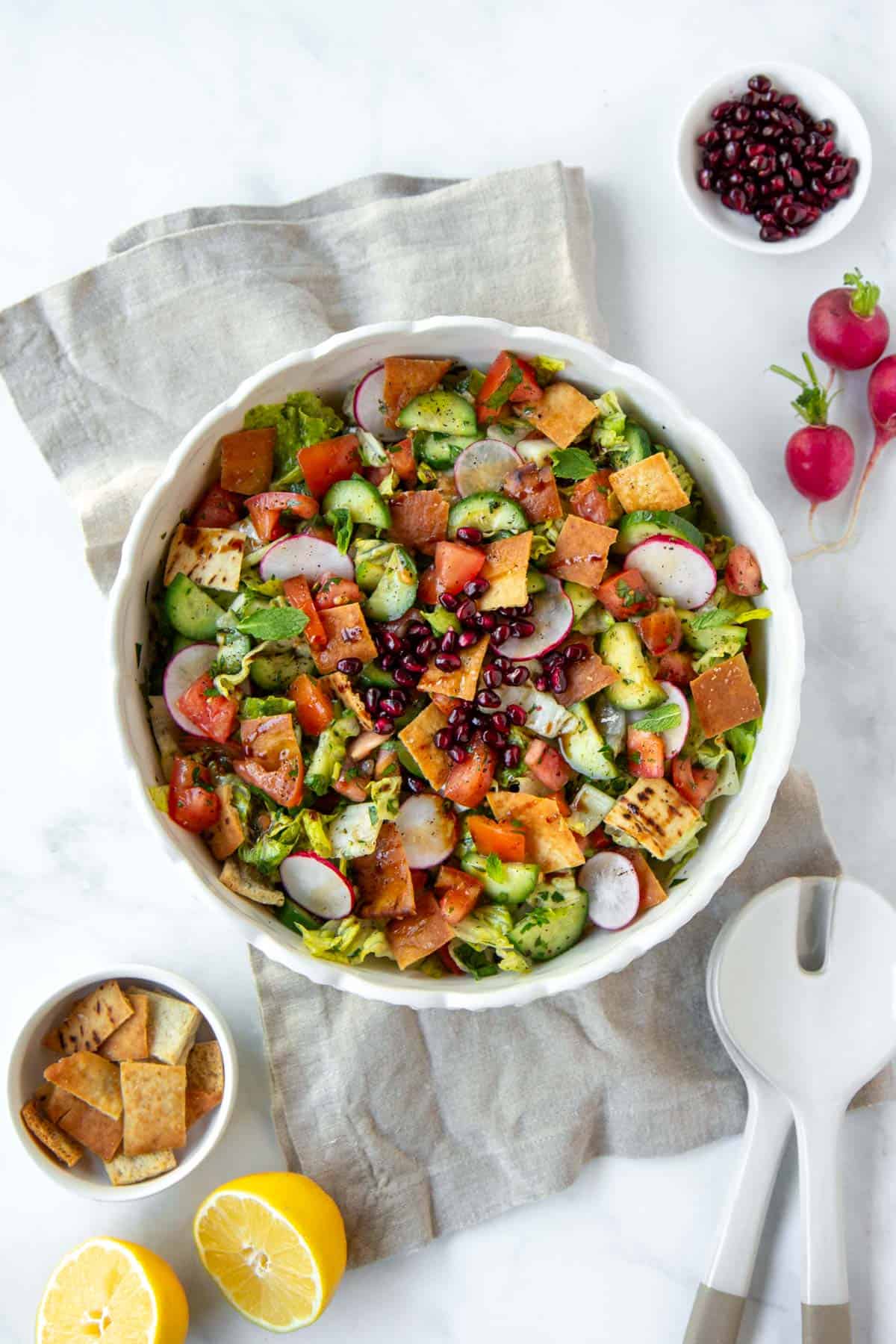 Fresh fattoush salad with radishes, cucumbers, tomatoes, pomegranate seeds, and pita chips in a white bowl.