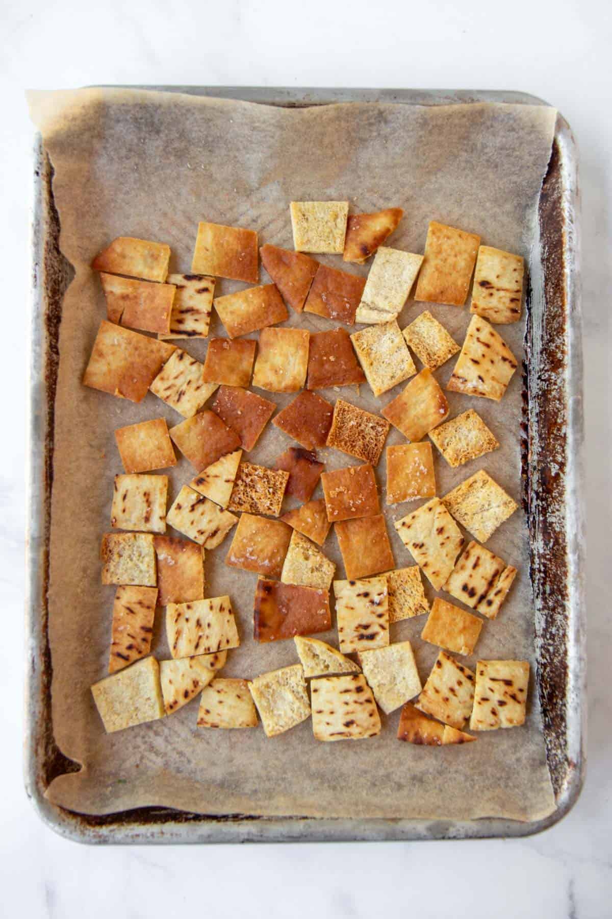 Golden baked pita chips on baking sheet with parchment paper, ready for serving.